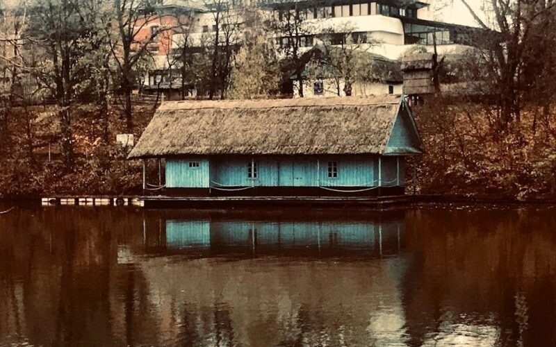 Vintage turquoise wooden bathing pavilion floating on a tree-lined lake
