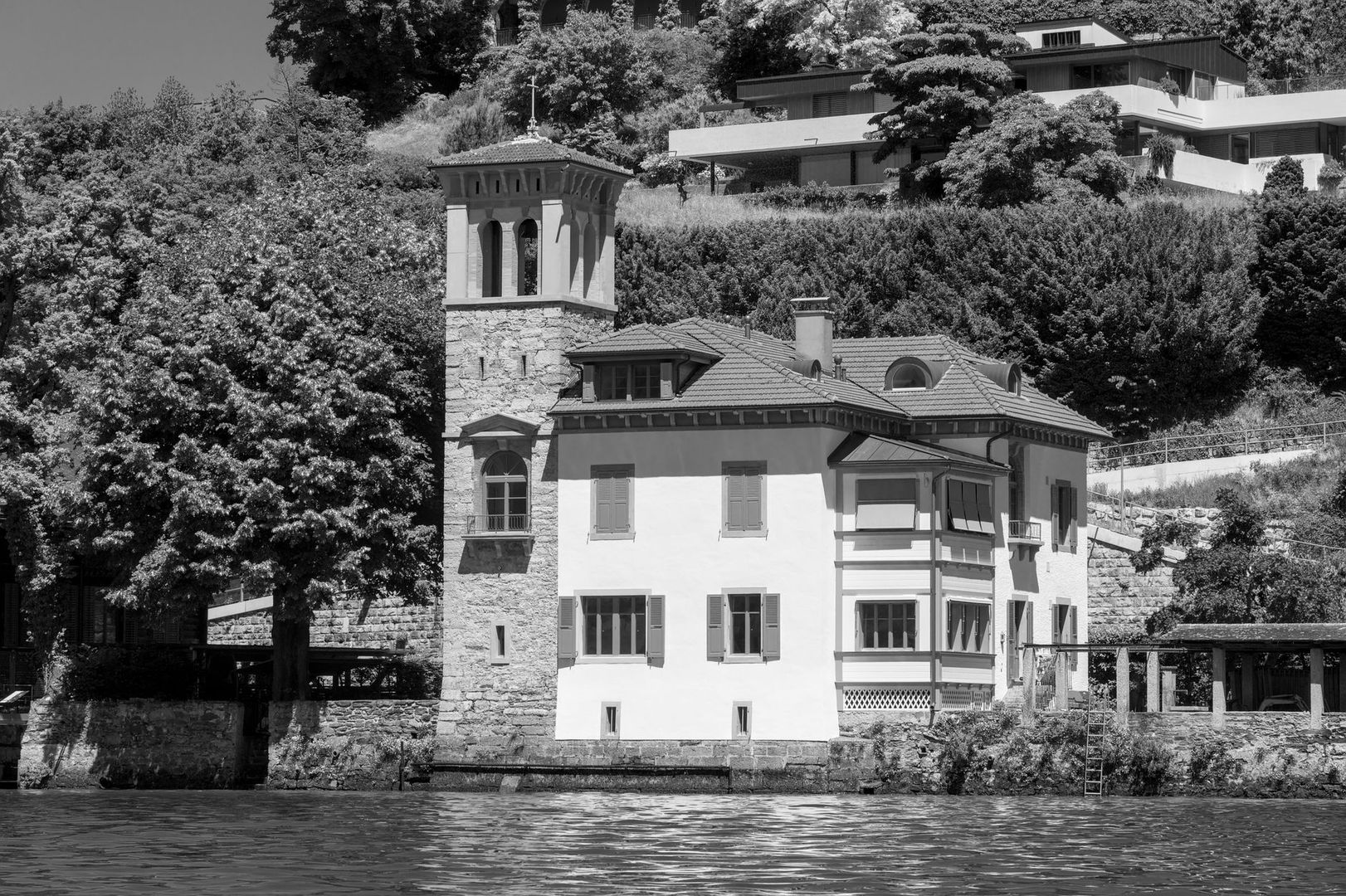 Historic lakeside building with tower and modern homes above the water